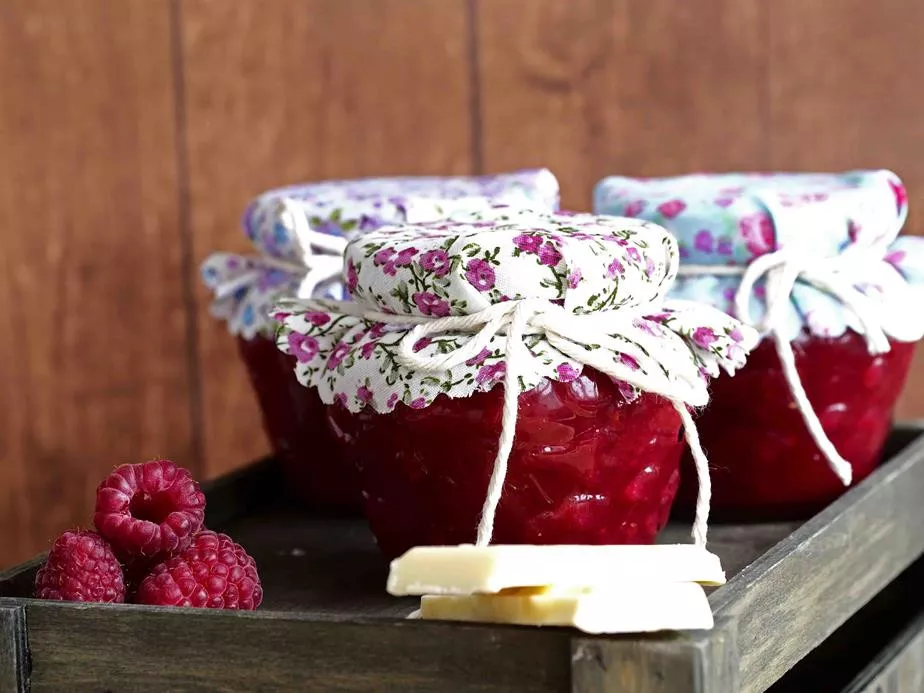 gładki dżem malinowy z białą czekoladą w słoiczkach na drewnianej tacy, maliny i czekolada biała obok - Wszystkiego Słodkiego