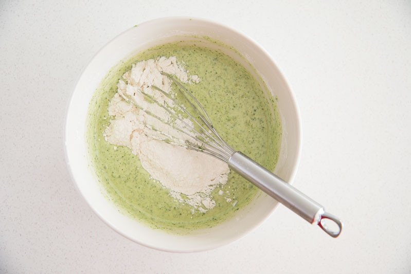 ciasto szpinakowe w misce z dodaną mąką, wymieszane rózgą kuchenną