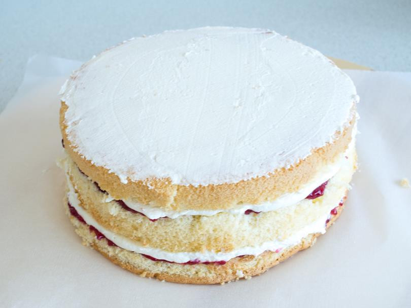 trzy blaty biszkoptu przełożone konfiturą malinową i białą częścią kremu śmietankowego z cienką warstwą tego kremu również na wierzchu tortu