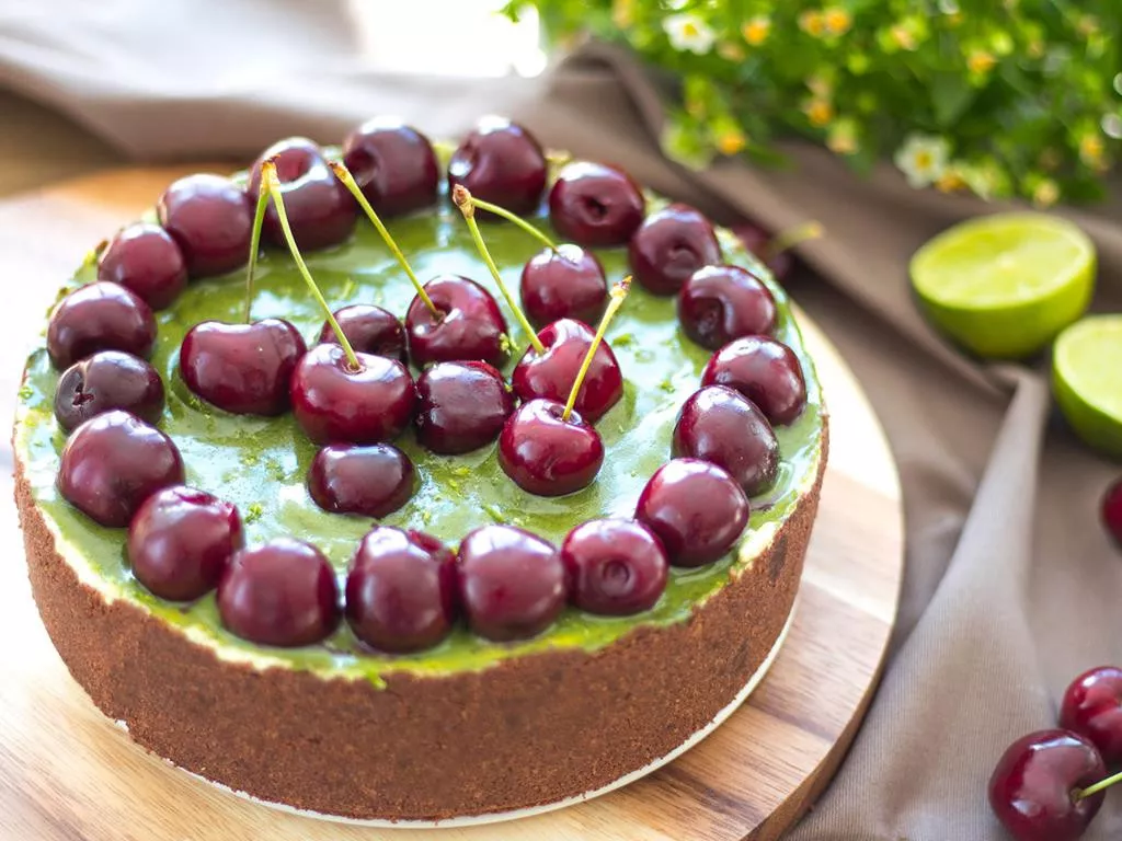 limonkowy sernik z herbatą matcha na spodzie z herbatników z kakao, zieloną polewą z białej czekolady i matchy, udekorowany czereśniami oraz skórką startą z limonki - Wszystkiego Słodkiego