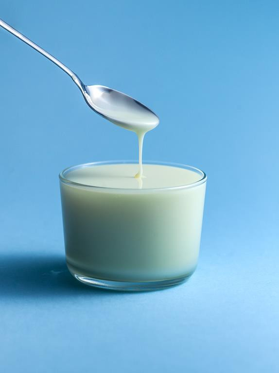 Mleko skondensowane w szklance w trakcie nabierania go łyżką.