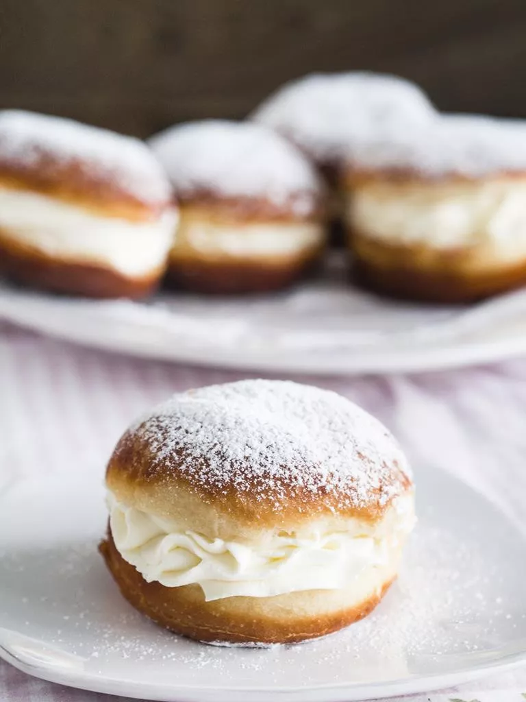 Pączki z bitą śmietaną i cukrem pudrem na talerzyku - Wszystkiego Słodkiego