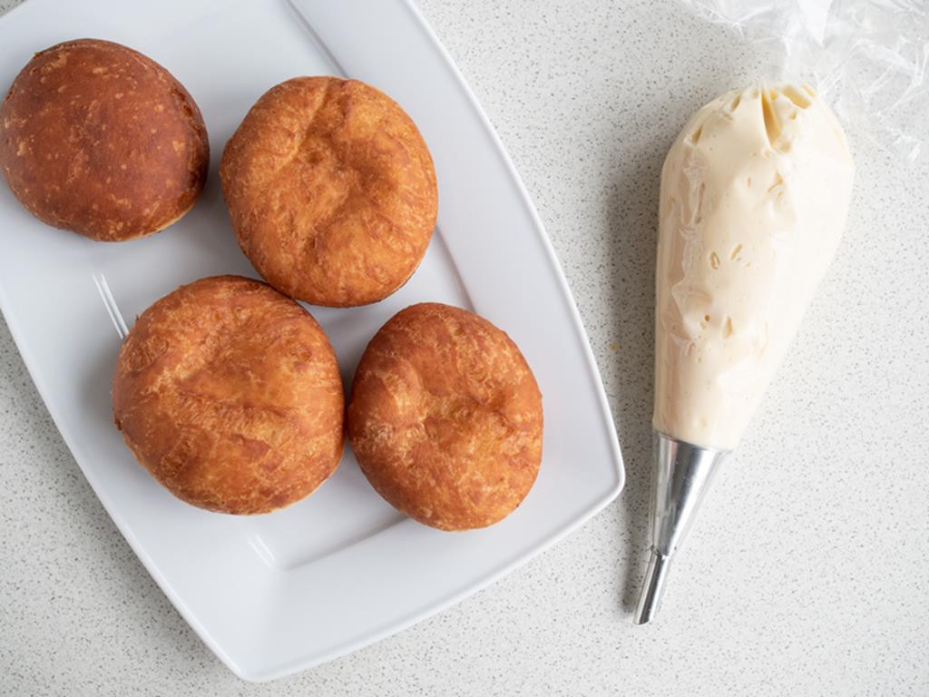 usmażone pączki na talerzu oraz budyń waniliowy do nadziewania pączków w rękawie cukierniczym z końcówką do nadziewania