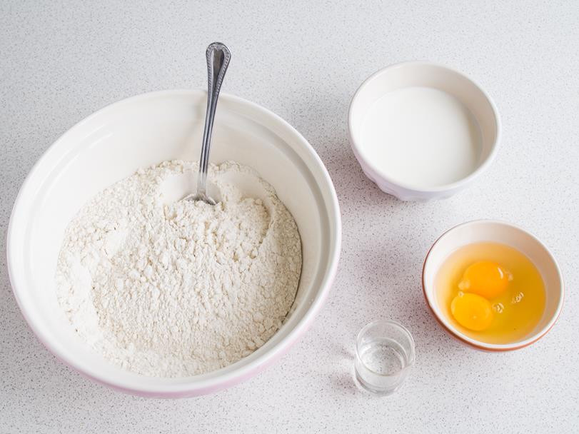 mąka wymieszana z drożdżami w misce, obok jajka i mleko w osobnych miseczkach i spirytus w kieliszku