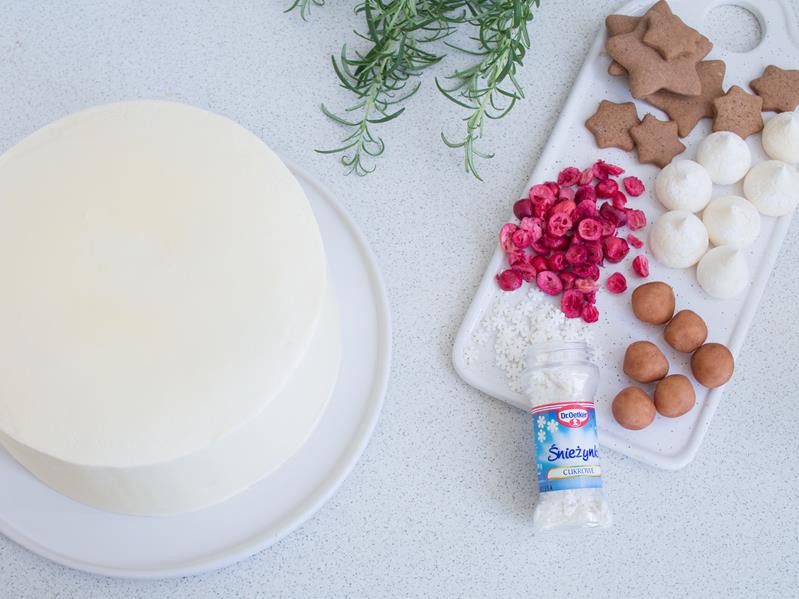 tort makowy obłożony kremem maślanym, obok dekoracje - pierniczki, kartofelki marcepanowe, świeży rozmaryn, liofilizowana żurawina, mini bezy oraz posypka śnieżynki od dr. oetkera