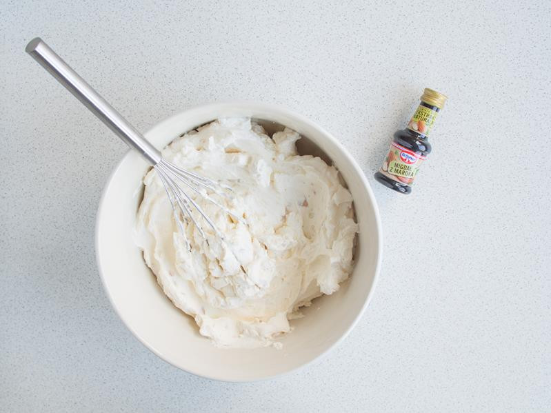 krem śmietankowy z kawałkami marcepanu w misce z rózgą kuchenną, obok ekstrakt migdałowy dr. oetkera