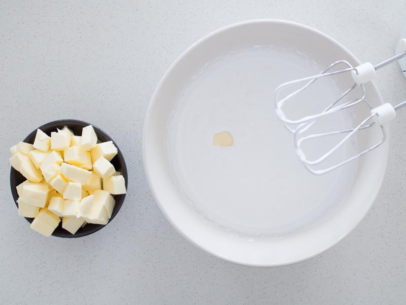 białka ubite z cukrem mikserem na bezę, obok miseczka z kawałkami masła