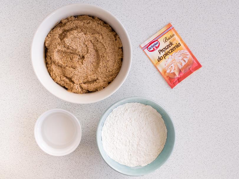 woda, mąka pszenna oraz masło utarte z cukrem kokosowym i jajkami w osobnych miskach, obok opakowanie proszku do pieczenia dr. oetkera