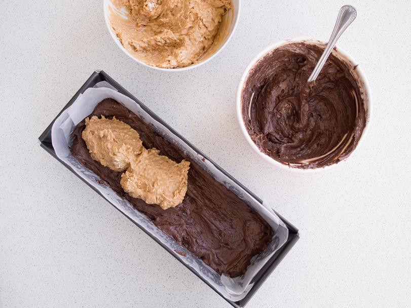 dwie miski z jasnym ciastem na babkę z wiórkami kokosowymi oraz ciemnym ciastem na babkę z kakao, obok keksówka z wyłożoną na dno warstwą ciasta z kakao i na niej warstwą z jasnego ciasta