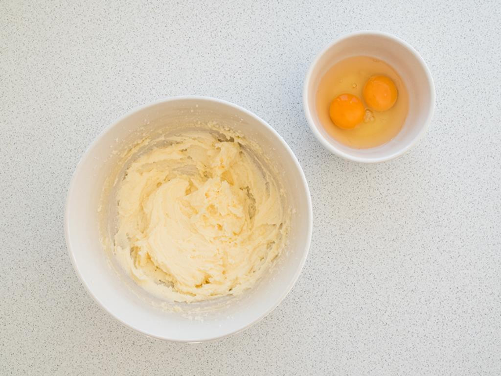 masło utarte z cukrem w miseczce, obok dwa jajka w drugiej miseczce
