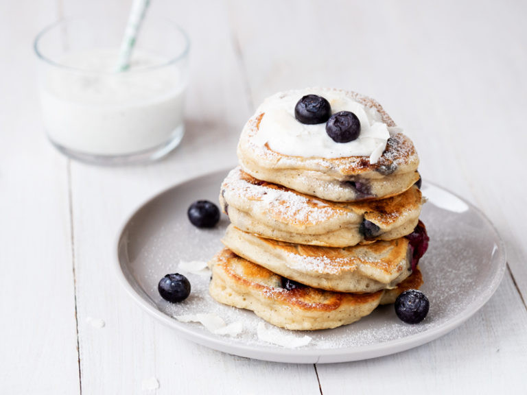 Pancakes z owocami, podane na talerzyku z jogurtem kokosowym, borówkami i cukrem pudrem - Wszystkiego Słodkiego