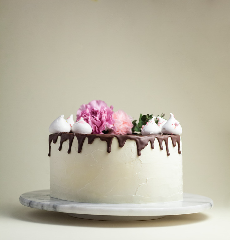 Biały tort Drip Cake z polewą czekoladową, bezikami i kwiatami