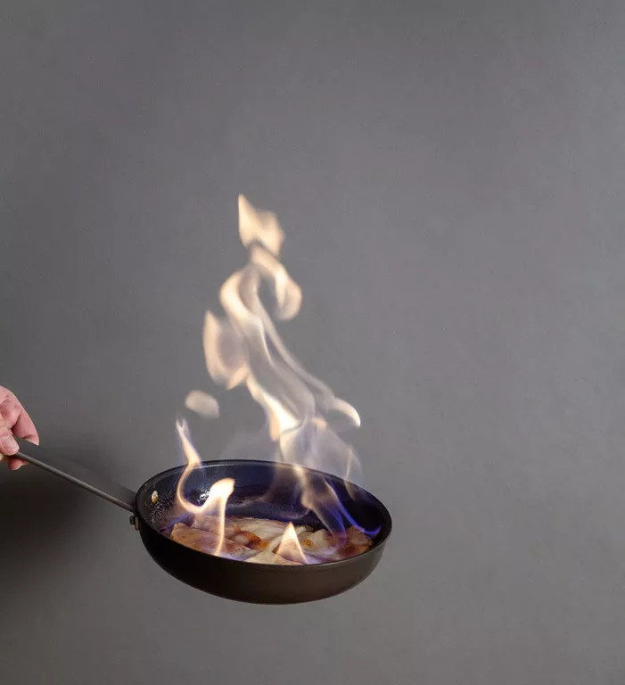 Flambirowanie Crêpes Suzette na patelni czyli polewanie naleśników wysokoprocentowym alkoholem i podpalanie ich. Nad patelnią unosi się ogień.