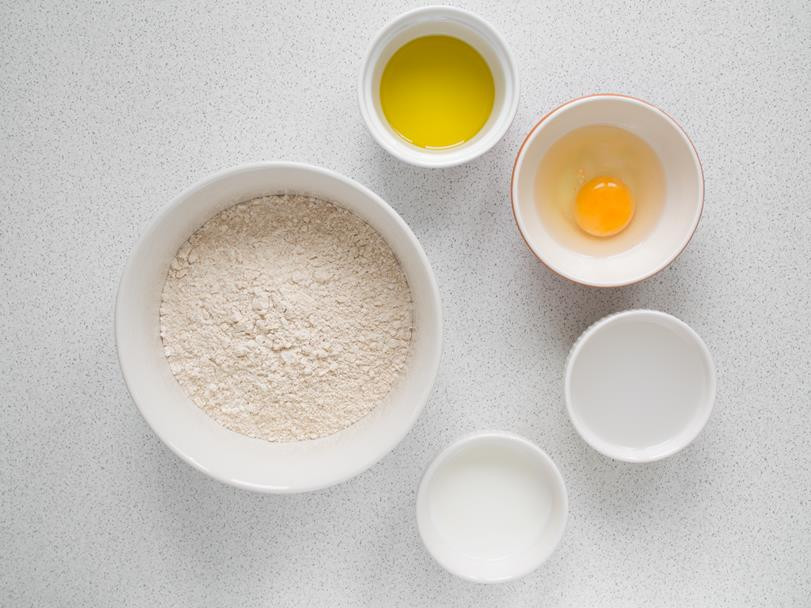 suche składniki wymieszane w misce oraz mokre składniki w osobnych miseczkach: oliwa, jajko, ciepła woda, mleko