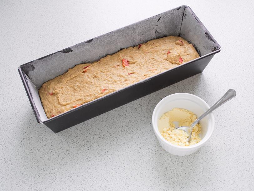 ciasto na chleb paprykowy wyłożone w formie keksówce, obok miseczka z mąką kukurydzianą i łyżeczką