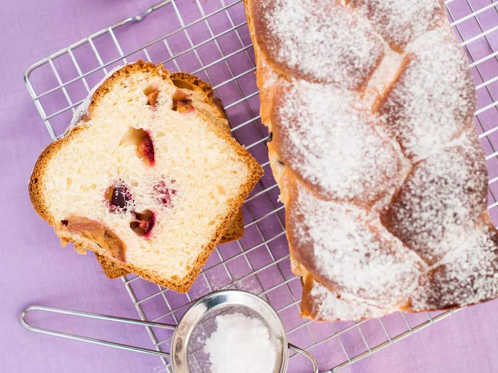 puszysta drożdżówka z warkoczem i śliwkami posypana cukrem pudrem na kartce do studzenia - wszystkiego słodkiego