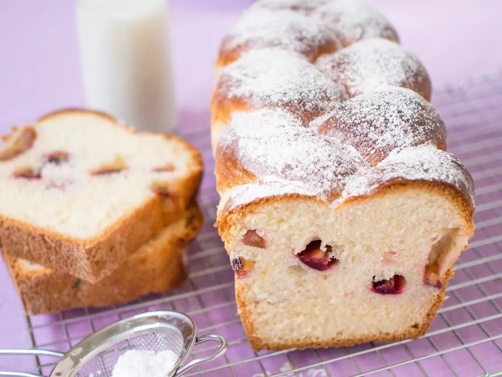 puszysta drożdżówka z warkoczem i śliwkami posypana cukrem pudrem na kartce do studzenia - wszystkiego słodkiego