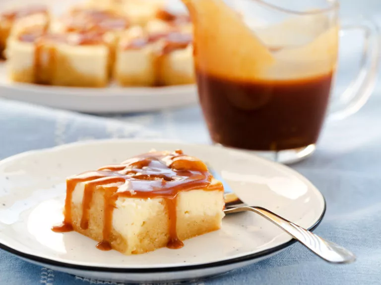 ciasto blondies z masą serową, masłem orzechowym i solonym karmelem podane na talerzyku z łyżeczką, w towarzystwie dzbanuszka z solonym karmelem - wszystkiego słodkiego