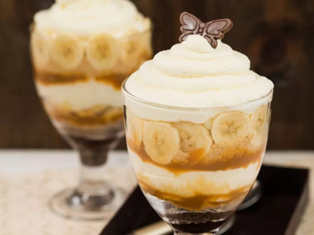 deser bananowy z kawałkami bananów, sosem toffi, bitą śmietaną i ciasteczkami w pucharku