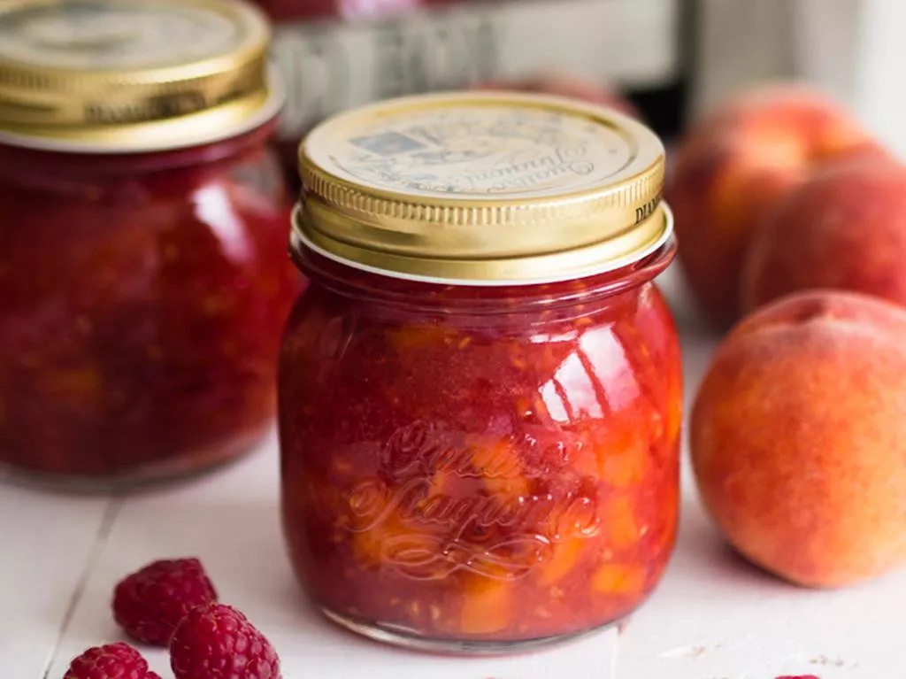 dżem brzoskwiniowo-malinowy z kawałkami owoców w słoiczkach, obok świeże brzoskwinie i maliny - wszystkiego słodkiego
