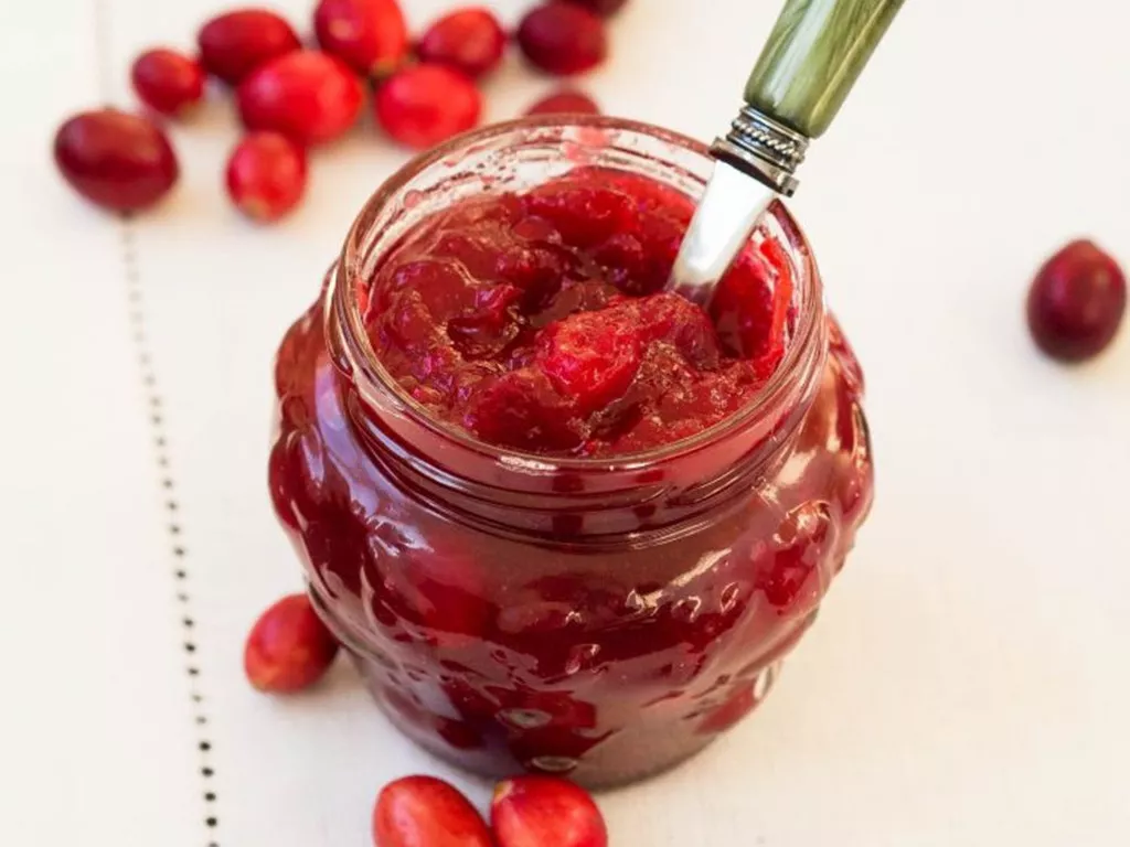 konfitura żurawinowa w słoiczku z łyżeczką i rozsypaną wokół na stole żurawiną - wszystkiego słodkiego