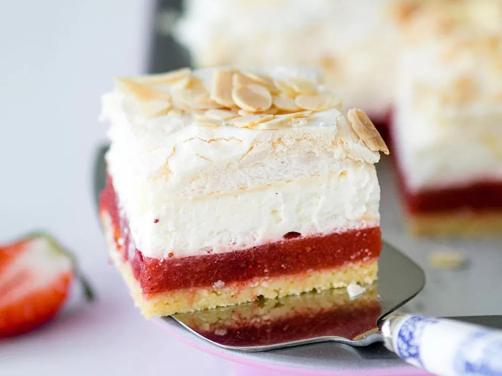 kawałek ciasta wiosenne trio na spodzie z ciasta ucieranego, z musem z rabarbaru i truskawek, z bitą śmietaną, bezą i płatkami migdałowymi - wszystkiego słodkiego