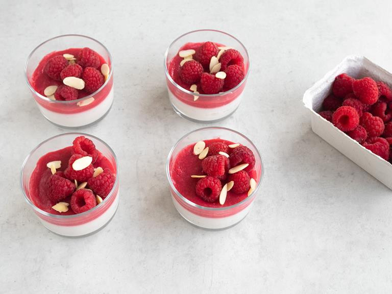Udekorowana panna cotta z sosem malinowym z płatkami migdałów i świeżymi malinami.