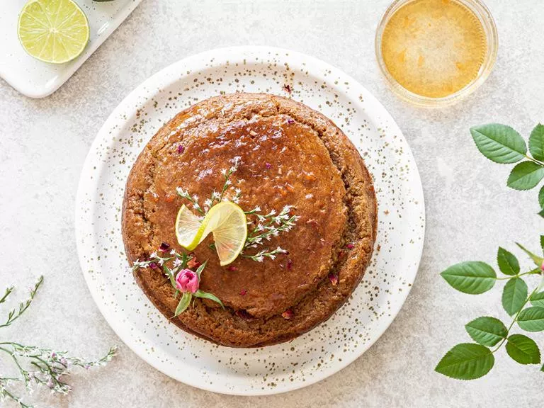 Ciasto z cukrem kokosowym i syropem grejfrutowym z różą, udekorowane plastrem limonki i świeżymi kwiatami.