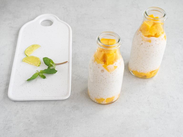 Pudding z tapioki z mango w szklanych pojemnikach. Obok świeże listki mięty i pokrojona limonka.