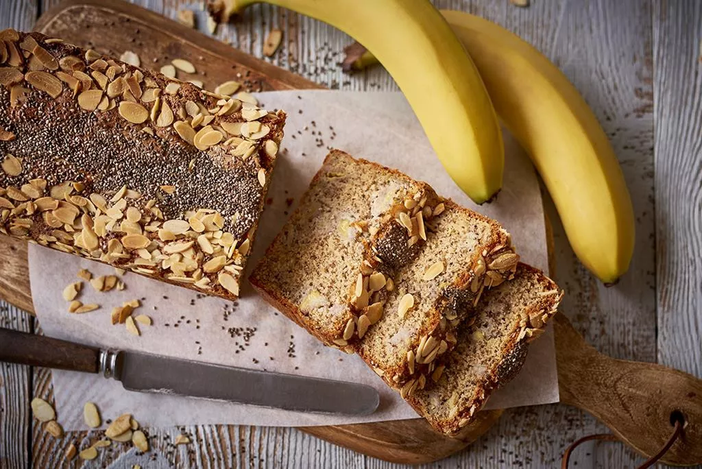 ciasto bananowo-migdałowe bez glutenu posypane nasionami chia i płatkami migdałów na desce
