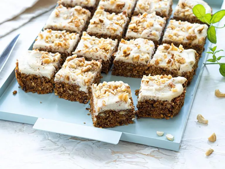 Wegańskie ciasto marchewkowe bez glutenu z kremem z nerkowców na niebieskiej paterze.