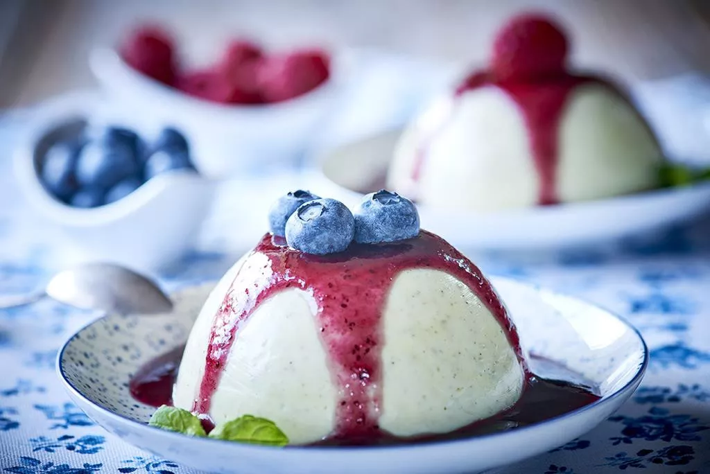 Waniliowo cytrynowa panna cotta z sosem i jagodamina twarogu podana z sosem owocowym i świeżymi owocami podana na deserowym talerzyku