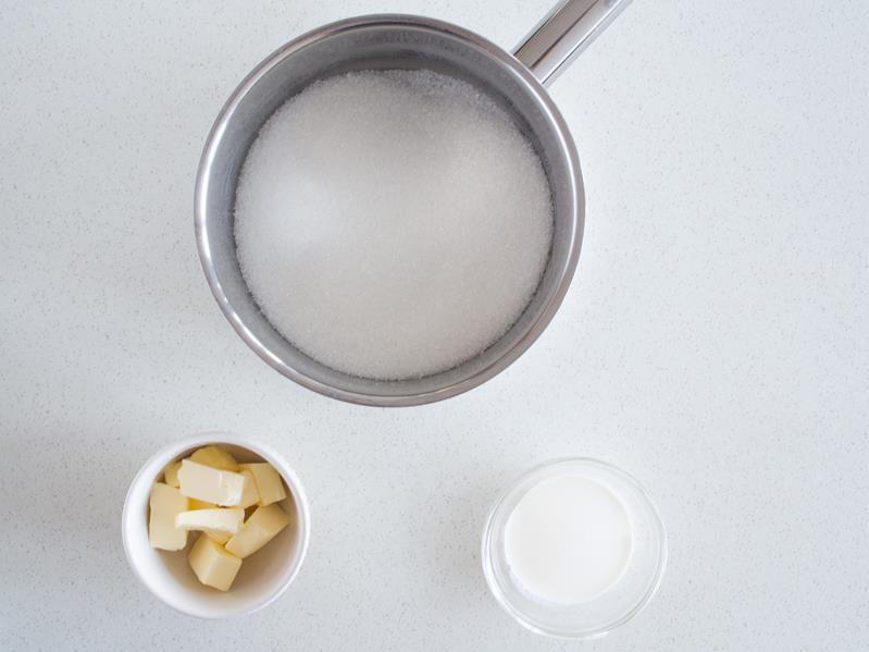 Cukier w garnku. Pokrojone masło i śmietanka w miseczkach.