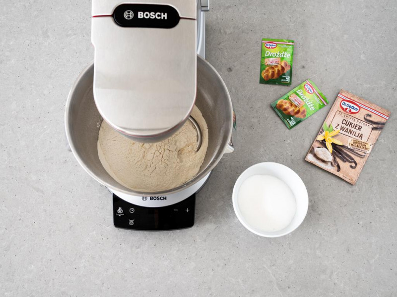 Robot kuchenny firmy Bosch z końcówką do ciasta drożdżowego. Obok drożdże suche, cukier z wanilią i cukier.