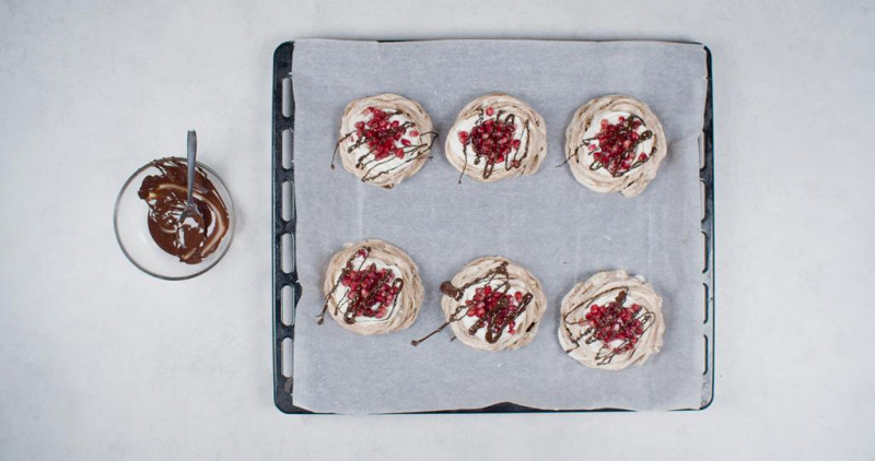 na blasze upieczone bezy czekoladowe z bitą śmietaną, posypane granatem i polane rozpuszczoną czekoladą