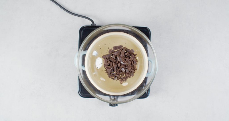 na palniku nad garnkiem szklana miska z pokrojoną czekoladą