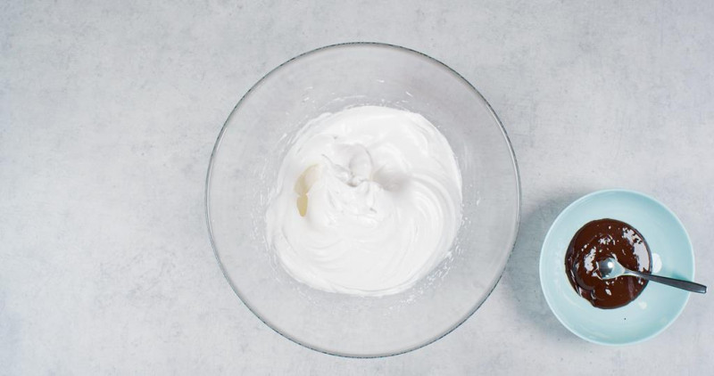 w szklanej misce śmietanka ubita z cukrem pudrem, obok w miseczce roztopiona czekolada