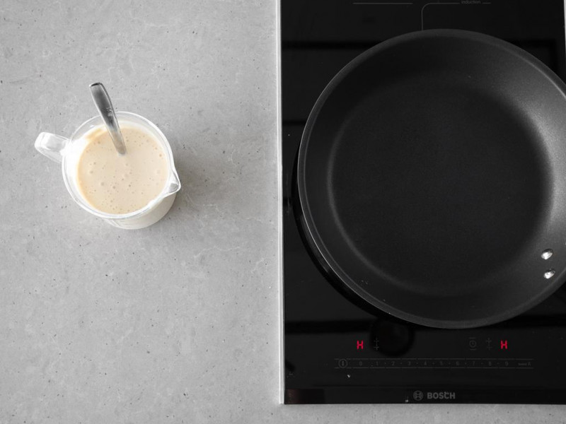 Patelnia na kuchence indukcyjnej firmy Bosch. Obok wymieszane ciasto na pancakes wegańskie.