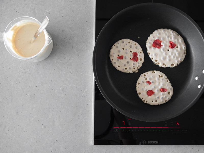 Ciasto na pancakes wegańskie i smażące się obok pancakes z malinami.