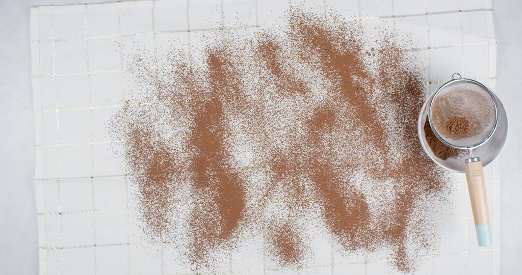 na kuchennej ściereczce oprószone kakao, miseczka z kakao oraz sitko