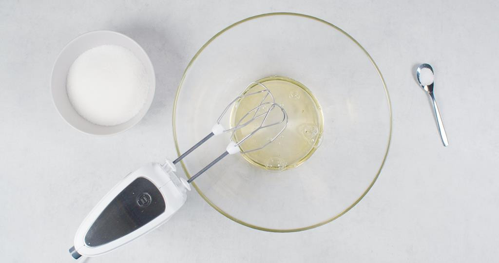 w szklanej misce białka przygotowane do ubijania mikserem, obok miseczka z cukrem i łyżeczka z solą