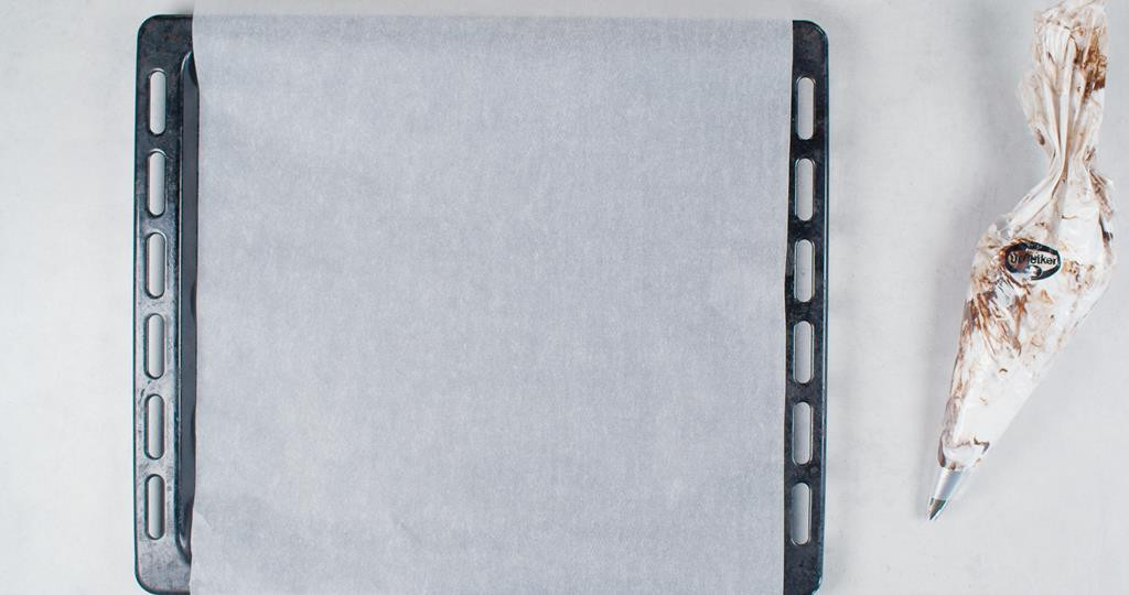 na blacie blacha z wyposażenia piekarnika z papierem do pieczenia, obok w worku cukierniczym masa na bezę czekoladową