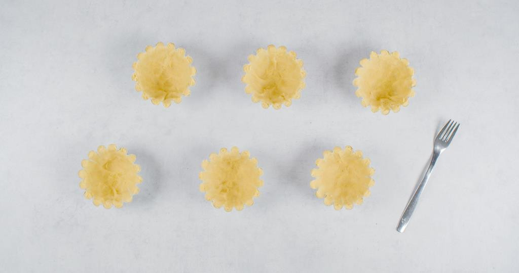 Foremki do tartaletek wyłożone ciastem ciastem kruchym, obok widelec