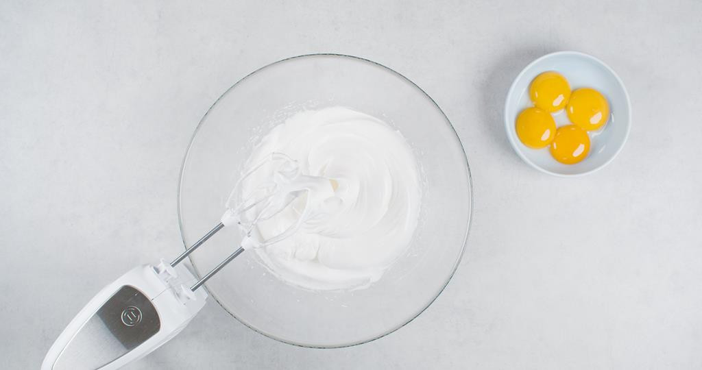 w szklanej misce ubite mikserem białka z cukrem, obok żółtka w miseczce