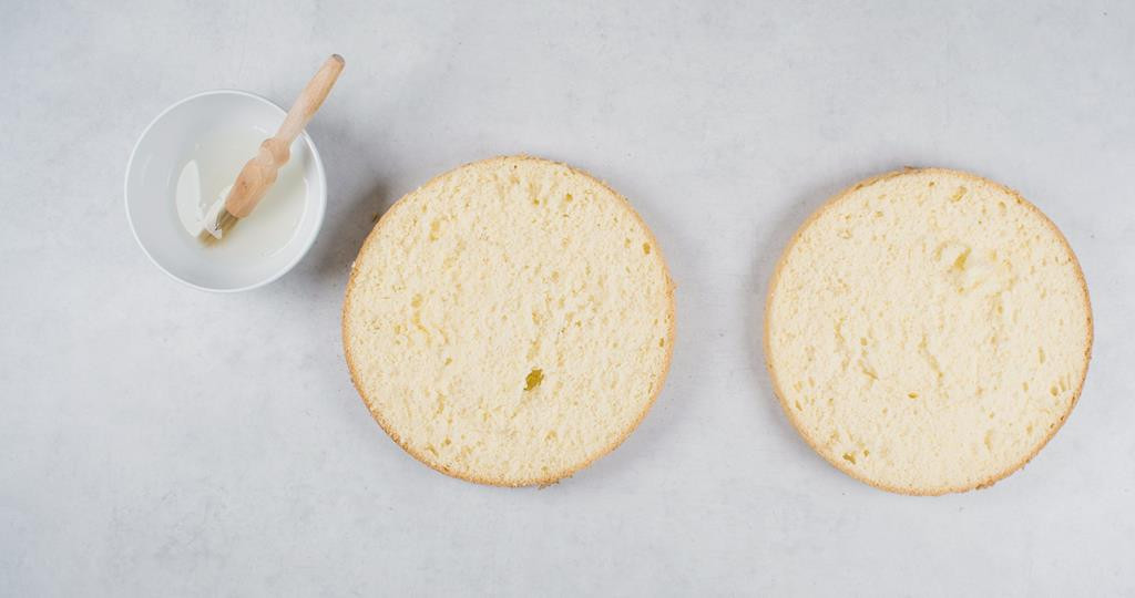 upieczony i wystudzony biszkopt przekrojony na dwa blaty, obok miseczka z ponczem do nasączenia, to jest wodą wymieszaną z sokiem z cytryny