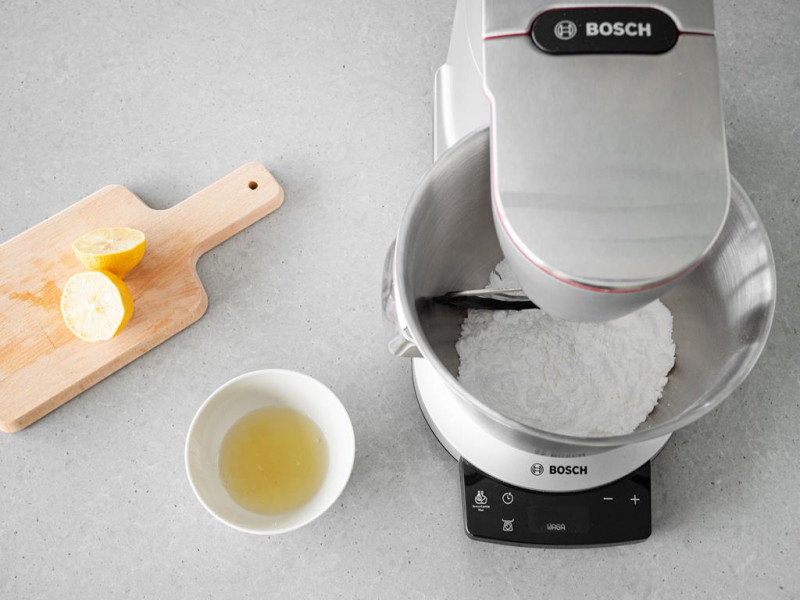 Cukier puder w misie robota kuchennego MUM firmy Bosch. Obok przekrojona cytryna i w miseczce białka.