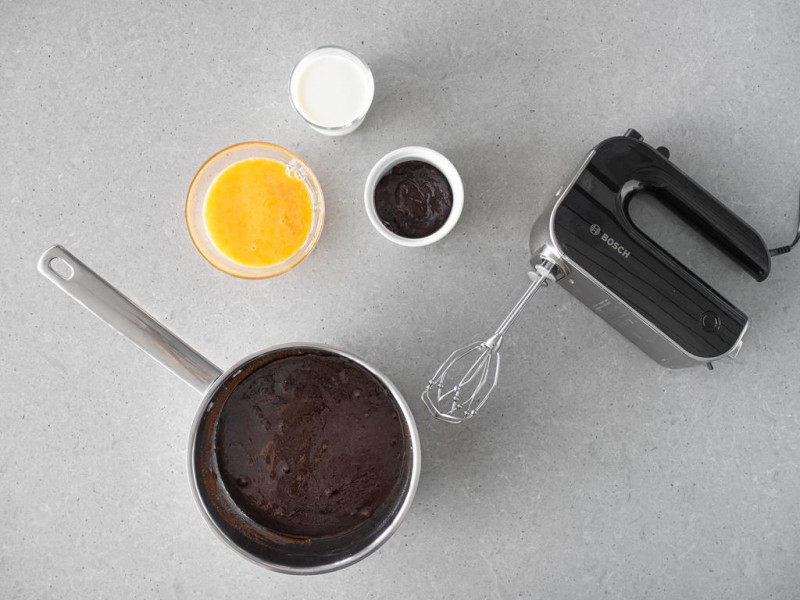 W garnku masa miodowo-korzenna, obok mikser ręczny firmy Bosch, jajka, powidła śliwkowe i mleko.