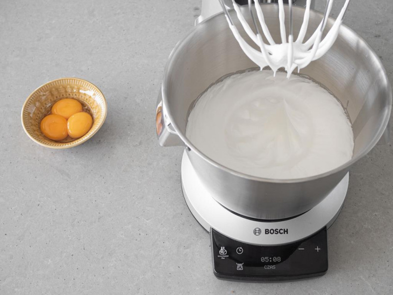 Ubite białka z cukrem w misie robota kuchennego MUM firmy Bosch. Obok żółtka w miseczce.