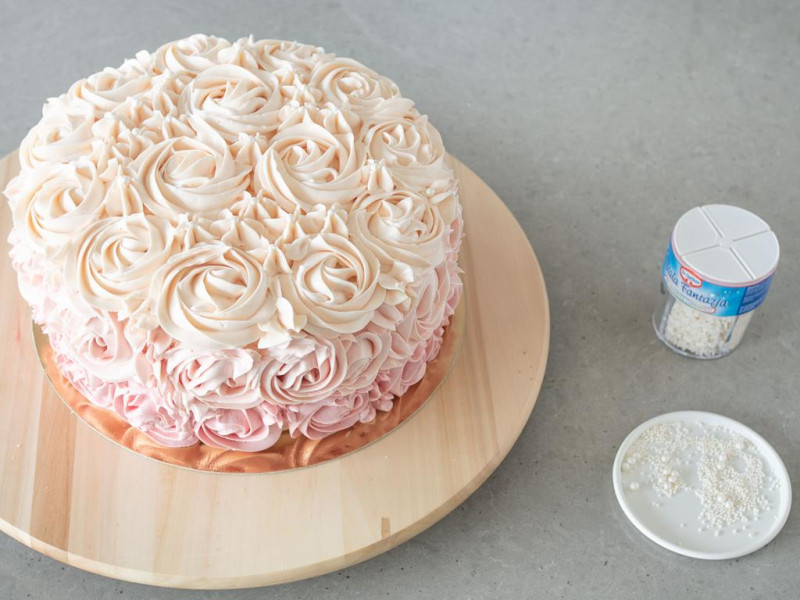 Gotowy tort ombre rose cake na drewnianej paterze. Obok mix dekoracji cukrowych Biała Fantazja.