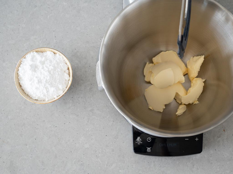 Wegańskie masło w misie robota kuchennego firmy Bosch. Obok cukier puder w miseczce.